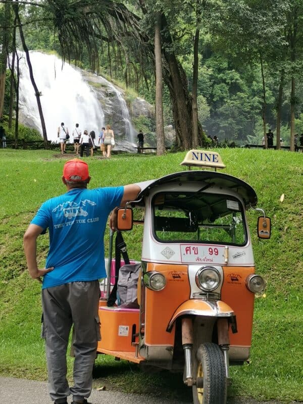 A man standing next to a Tuk Tuk looking at a waterfall