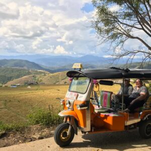 A Tuk Tuk on a small country road with mountains in the background