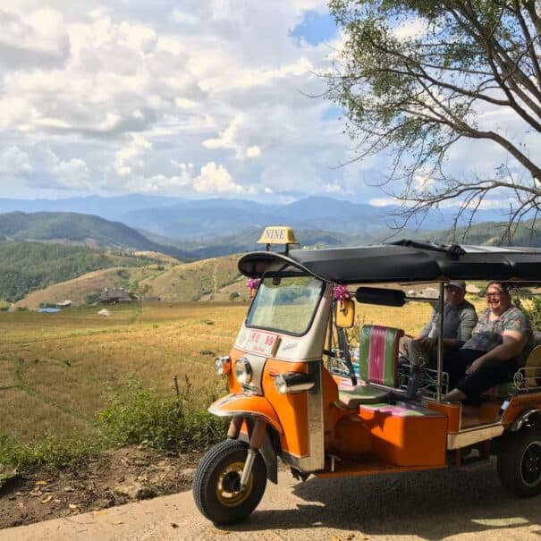 A Tuk Tuk on a small country road with mountains in the background