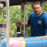 A Thai man standing next to a Tuk Tuk
